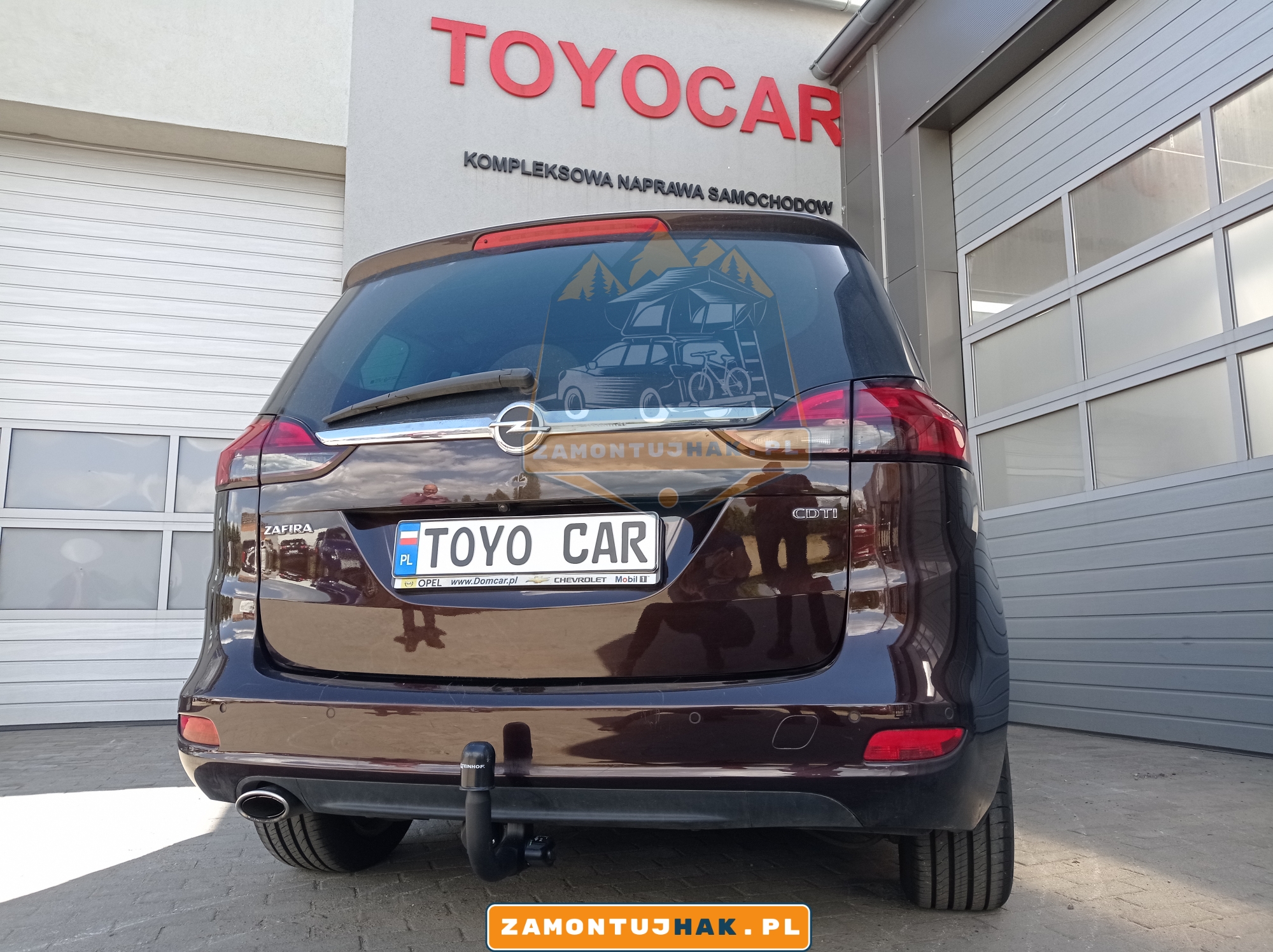 Zdjęcie Opla Zafiry z zamotowanym hakiem Steinhof, zdjęcie zrobione z tyłu samochodu, na tle serwisu zamontujhak.pl 